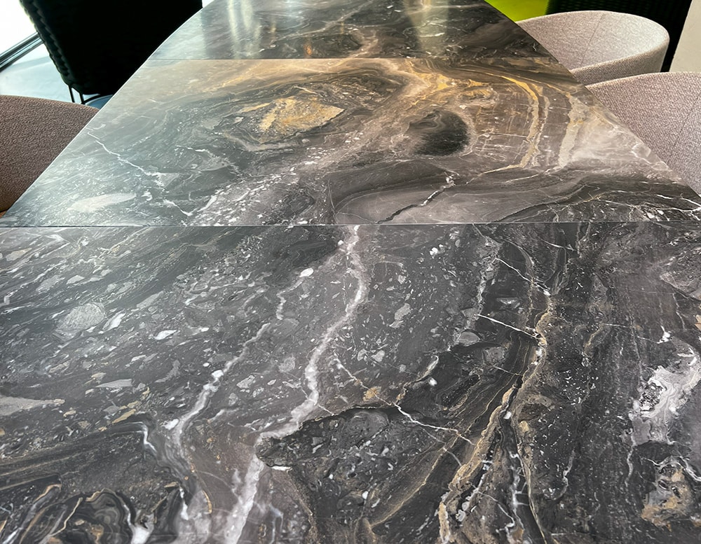 View from above of an extendable dining top in black marble leathered stone with a base with castor dark bronze.
