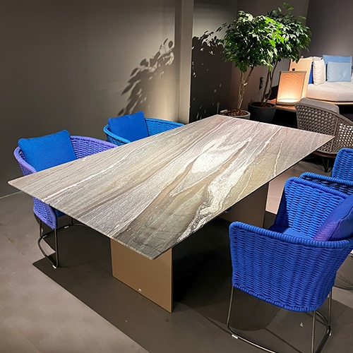 An extendable dining table made of natural stone with a rectangular top with a clear brown color winter wood leather