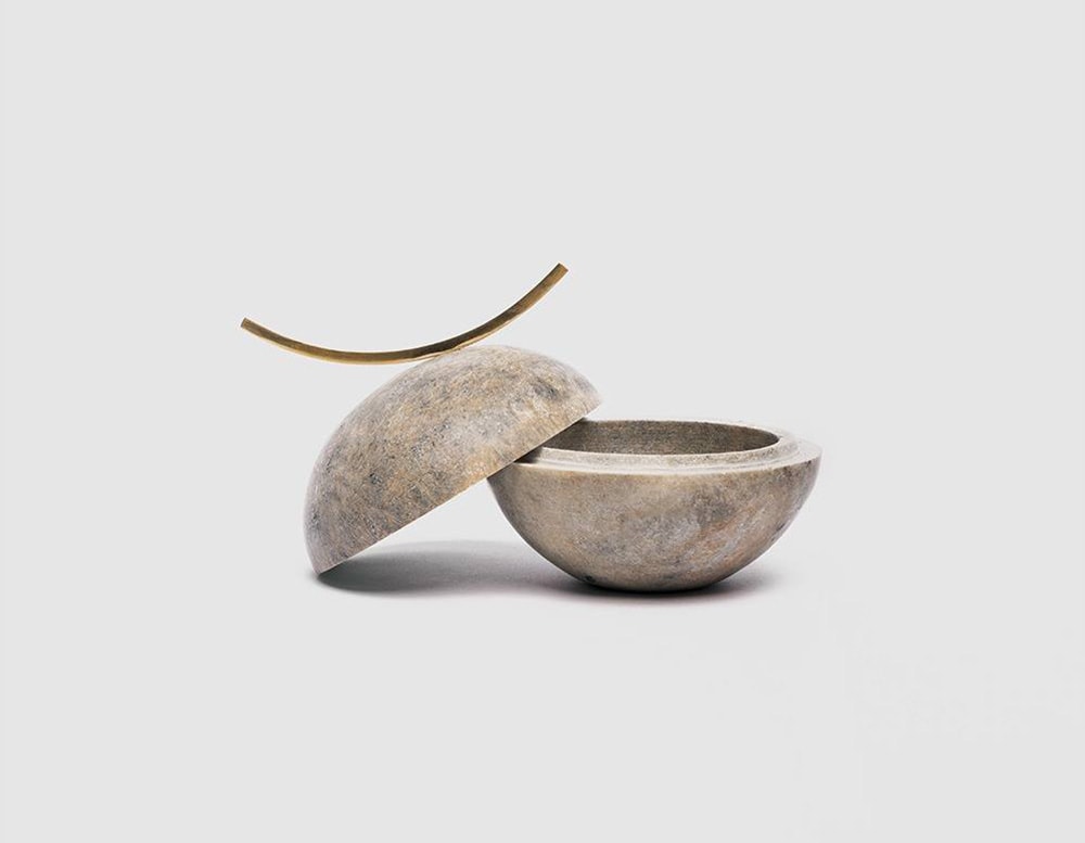 small soapstone vessels with different shades of gray and brass finishes, used to store small precious objects in a white background.