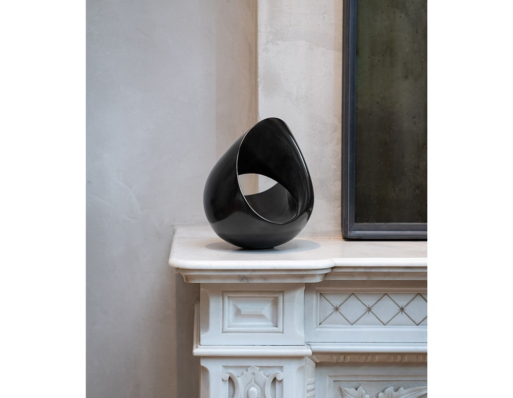 small black bronze sculpture in the shape of a drop and a particular round aperture in the middle in a living room.