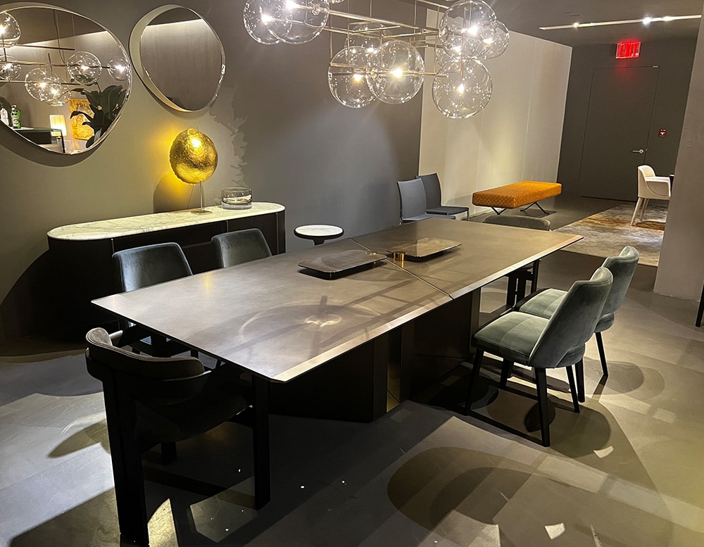 Dining table of black marble structure with painted bronze glass top, beveled edges on two sides of the top with junction detail between tops in Satin Brass, and bright stainless steel bottom