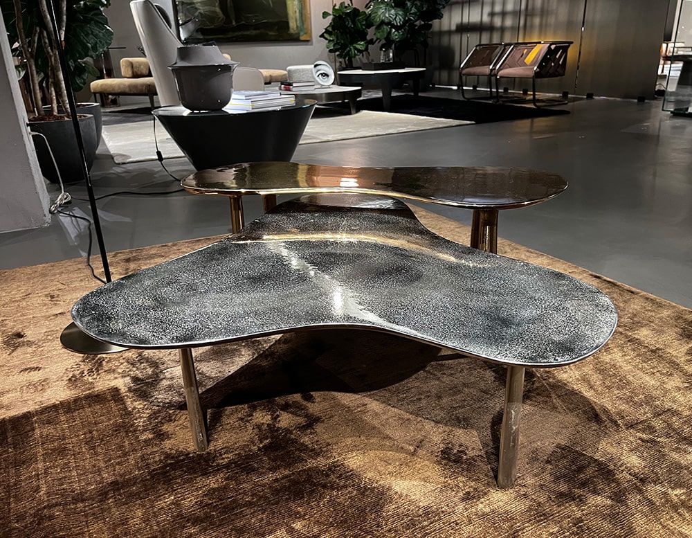 two sand-cast coffee tables in black brass finish with white details and gold-colored metal legs