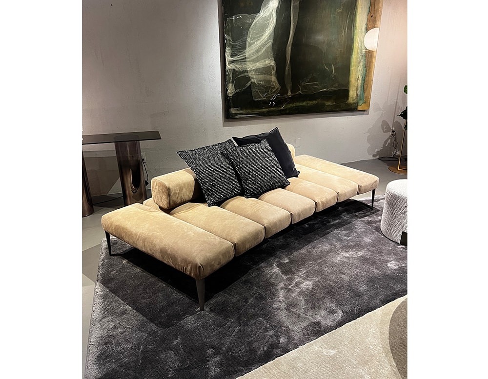Sofa with backrest covered in beige leather with 7 divisions, thin black legs and black decorative cushions