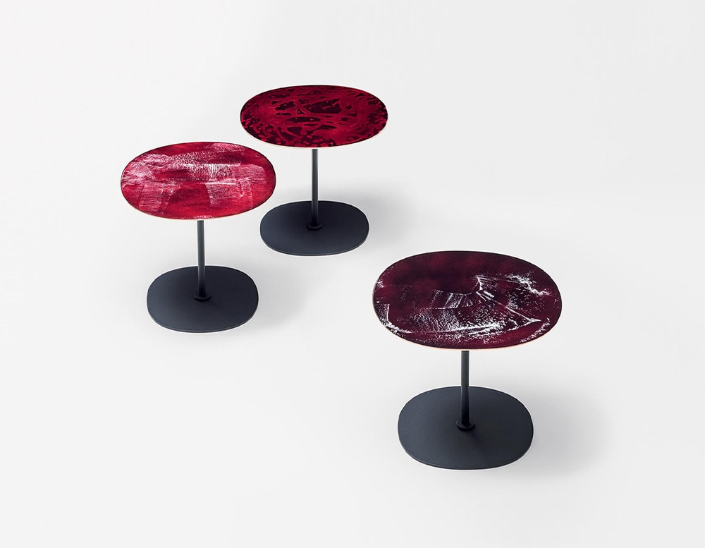 Three side tables with black base and tops with different textures and shades of red