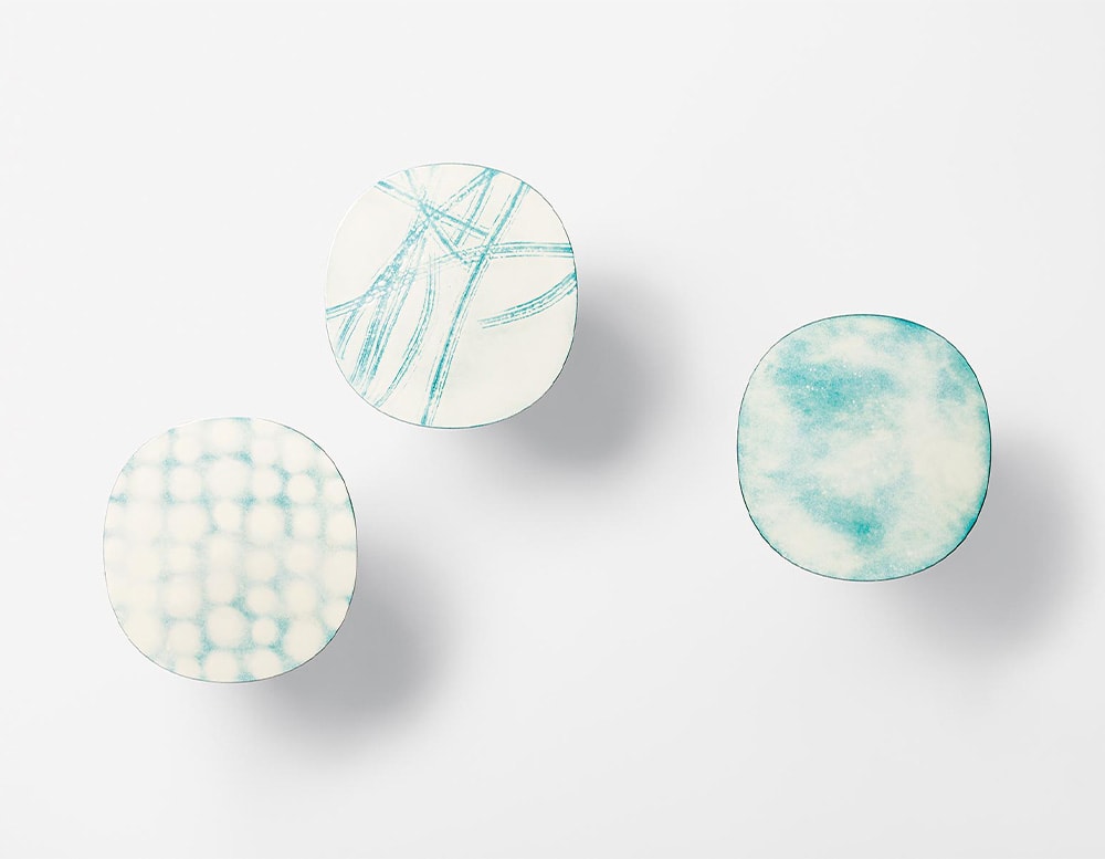 Three side tables seen from above with beige color tops with aquamarine color decorations