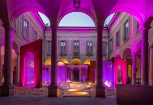 A grand courtyard bathed in vibrant pink and purple lighting, highlighting classical architecture with arched columns and intricate details