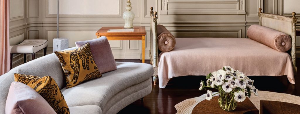 A close-up of an elegant living space, highlighting a curved pastel sofa, a pink chaise lounge, a wooden side table, and intricate wall moldings