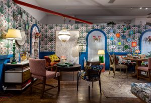 A vibrant and eclectic living space featuring bold floral wallpaper, arched blue doorways, vintage-inspired furniture, and warm lighting