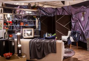 A luxurious living space with a neutral-toned sofa, dark draped fabric, elegant shelving, and ambient lighting creating a moody atmosphere