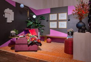 A vibrant interior with geometric wall patterns in pink and purple, a cozy red armchair with patterned upholstery, and modern lighting, creating a bold and stylish atmosphere.