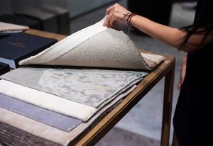 A person flips through a collection of elegant fabric samples displayed on a wooden table, showcasing various textures and patterns