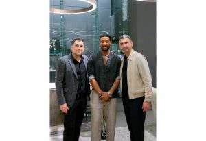 Three men posing in a modern, well-lit interior with a sleek contemporary design, featuring reflective surfaces and ambient lighting