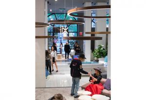 A lively showroom with people engaging in conversations and exploring modern furniture, illuminated by unique hanging light fixtures
