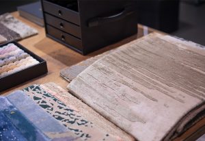 An antique book with handwritten text lies open on a wooden table, accompanied by fabric samples and a black storage box