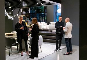 A group of elegantly dressed individuals engaged in conversation inside a modern showroom, surrounded by luxurious furniture and ambient lighting