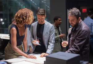 A group of people engaged in conversation around a table, examining design materials in a modern, well-lit setting with a social ambiance