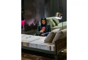 A woman sits on a stylish modern sofa in a dimly lit lounge, focused on her phone, with cozy furnishings and ambient lighting around her