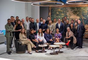 A large group of elegantly dressed individuals posing in a modern, well-lit interior space with stylish furniture and artistic decor in the background