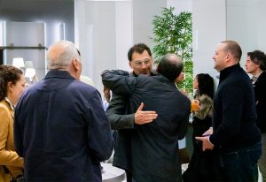 A group of people warmly greeting each other at an indoor event, with handshakes and smiles exchanged in a modern setting
