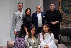 A group of six elegantly dressed individuals posing in a modern interior setting with stylish furniture and contemporary decor in the background