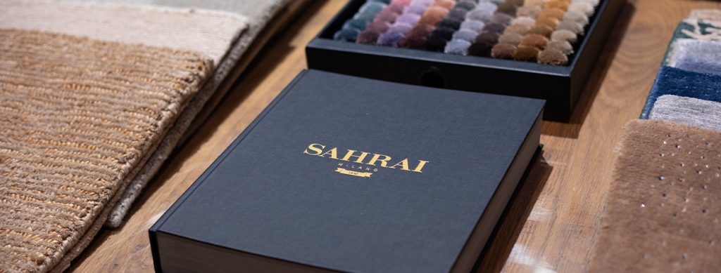 A close-up of a black Sahrai box on a wooden table, accompanied by a selection of colorful fabric samples neatly arranged
