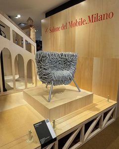 A showroom display featuring a designer armchair with an intricate textured surface set on a wooden platform with an elegant architectural backdrop