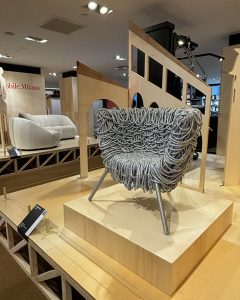 A showroom display featuring a unique designer armchair with an intricate textured surface set on a wooden platform in a modern exhibition space
