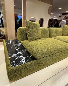 A green sofa with a built-in black marble side table is partially visible in a public space with blurred figures in the background