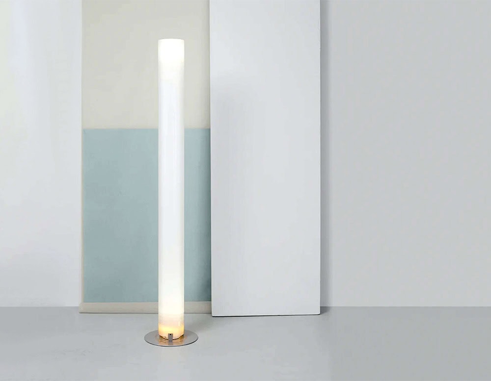 Flos Stylos floor lamp offers soft diffused light through a sleek white column resting on a polished metal base perfect for minimalist interiors with a serene ambiance.