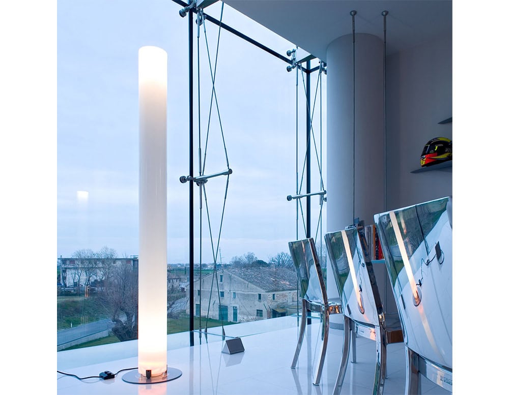 Flos Stylos floor lamp emits a warm vertical glow through its cylindrical diffuser creating a striking contrast with contemporary interiors and expansive glass views.