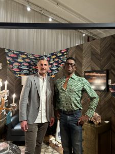 Two guests pose together in a stylish showroom corner featuring patterned wallpaper, ambient lighting, and elegant furniture accents.