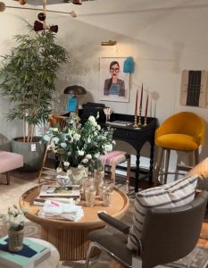 A cozy, eclectic vignette with a mustard velvet chair, vintage writing desk, and soft-toned seating. The floral centerpiece, gold candlesticks, and whimsical artwork add charm and personality to the space.