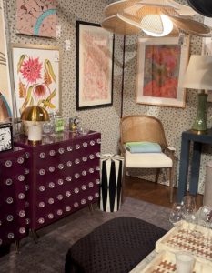 Bold and playful, this room pairs a plum cabinet dotted with glass knobs and a petal-like pendant light. Artworks pop against speckled wallpaper, while rattan, lacquer, and ceramics round out the vibrant, eclectic mix.
