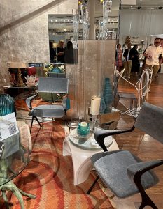 A sleek, contemporary lounge with velvet chairs, mirrored accents, and sculptural vases. The space pairs soft textures with reflective surfaces, highlighted by bold vertical lights and warm wood flooring.