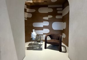 Bax brings quiet elegance with a low-profile armchair in chocolate suede. Set against graphic wall art, the scene is completed by delicate ceramic vases atop a wireframe table, forming a sculptural and serene composition.