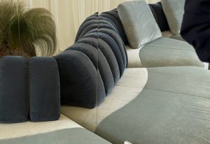 Showcases a sculptural modular sofa defined by plush, scalloped backrests in rich navy velvet. The contrasting pale sage seating creates a fluid, organic silhouette, while mirrored reflections and soft neutrals enhance the luxurious ambiance.