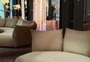 Curves in shimmering beige upholstery sit before mirrored panels. Soft contours meet reflective opulence. The reflection doubles the room’s elegance. A balance of subtle texture and architectural depth creates a serene but striking space.