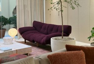 Ploum radiates comfort with its inviting plum-colored upholstery and plush, organic shape. The deep seat contrasts elegantly with natural accents like the white terrazzo planter and soft lighting, creating a serene lounge setting.