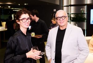 Guests enjoy drinks and conversation inside the warmly lit showroom, surrounded by elegant modern shelving and ambient design elements.