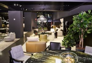 This upscale showroom pairs sleek, contemporary furnishings with sculptural lighting and lush greenery. Layered textures, curved forms, and soft neutral tones create a refined yet welcoming lounge environment.