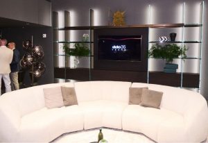 A cozy seating area with a white curved sofa is set against modern shelving and warm lighting during a showroom event.