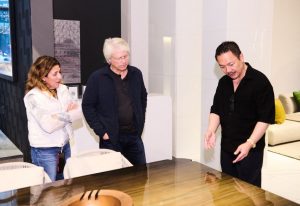 Guests gather around a polished wood table as a presenter discusses its design details in the showroom.
