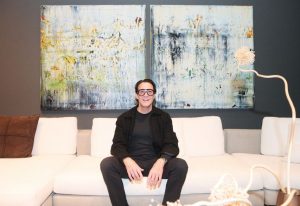 A guest relaxes on a soft white sectional, framed by abstract art and sculptural lighting in the elegant showroom setting.