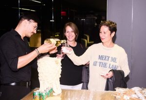 Two women enjoy drinks as wine is served at a warmly lit showroom bar, creating a lively and inviting social atmosphere.
