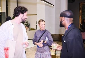 Three guests chat and smile inside a contemporary showroom lounge, surrounded by soft lighting, plush seating, and warm tones.