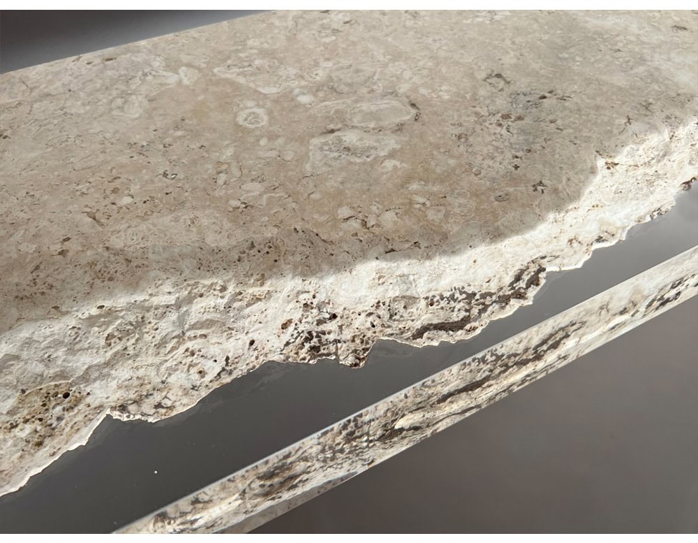 A close-up of the Rapolano Console Table reveals the raw travertine surface set against crystal-clear acrylic. The natural stone edge contrasts beautifully with the sleek transparent inlay, highlighting the table’s refined construction.