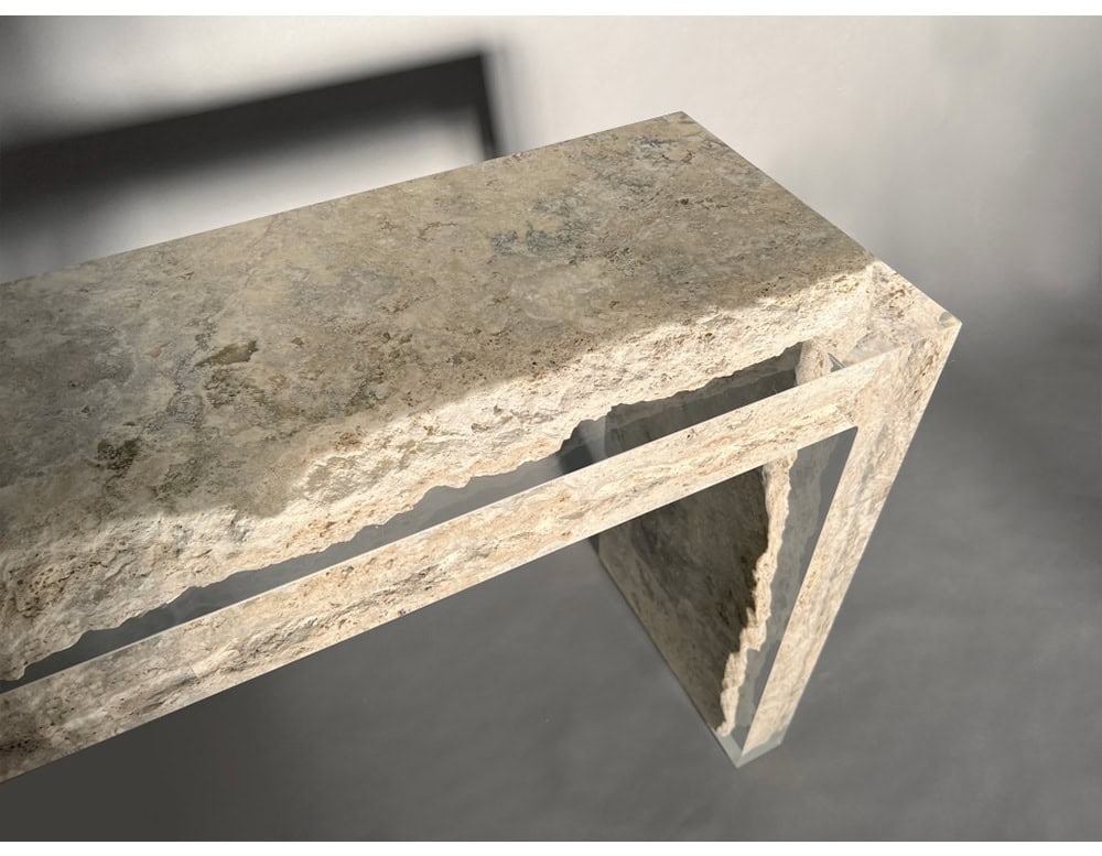 The Rapolano Console Table features raw travertine stone with organic textures, paired with sleek acrylic inserts that create a floating effect. The interplay of rough and smooth materials defines its sculptural design.