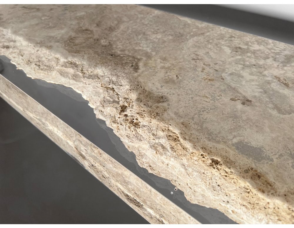 A close-up of the Rapolano Console Table top highlights the natural travertine’s raw texture, seamlessly intersected by a sleek acrylic inlay that adds a contemporary, polished contrast.