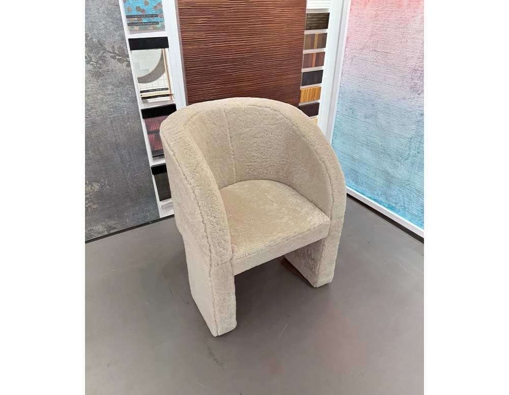 Bax Lazybones Armchair displays a softly contoured silhouette in a creamy upholstery with a cozy texture. The chair is placed in a sample-filled design setting, with varied panel textures and tones enhancing the neutral flooring.