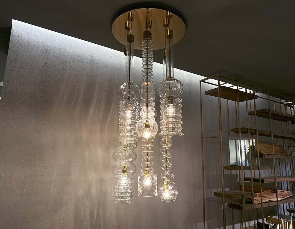 Praha Suspension Light features a striking cluster of textured glass pendants in various organic forms, suspended from a polished canopy to cast elegant reflections and ambient light throughout the space.